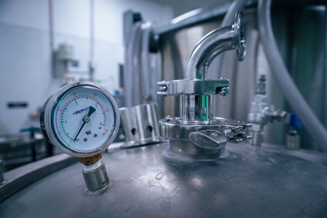 Close-up of a pressure gauge on a stainless steel tank in a sterile industrial setting, showcasing manufacturing technology.